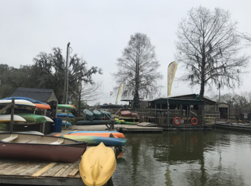 A dock with colorful kayaks and canoes on a foggy day, surrounded by trees and a small building.