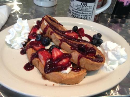 A plate of French toast topped with strawberries, blueberries, whipped cream, and berry sauce.