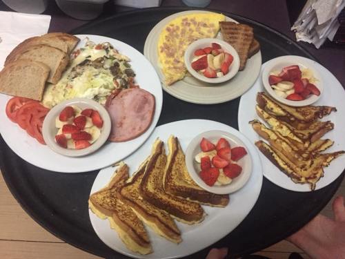 A tray with two plates: one with an omelette, toast, ham, and a veggie dish; the other with French toast and fruit.