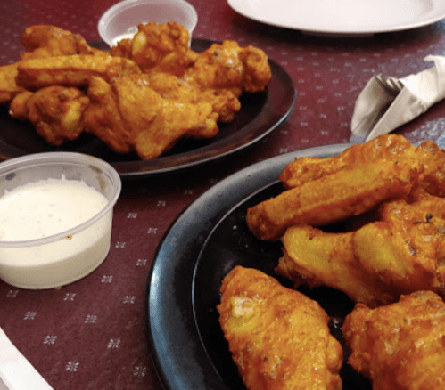 A close-up of two plates of spicy chicken wings with a side of dipping sauce.