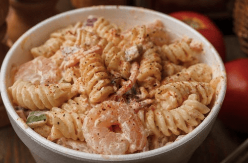 A bowl of creamy pasta salad with shrimp, vegetables, and seasoning, garnished with spices.