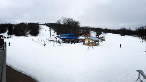 A snowy ski resort with a lodge, ski lifts, and skiers on the slopes under a cloudy sky.