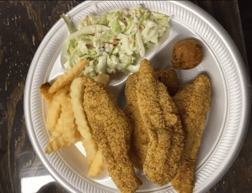 A plate with three fried fish fillets, crinkle-cut fries, coleslaw, and a hushpuppy.