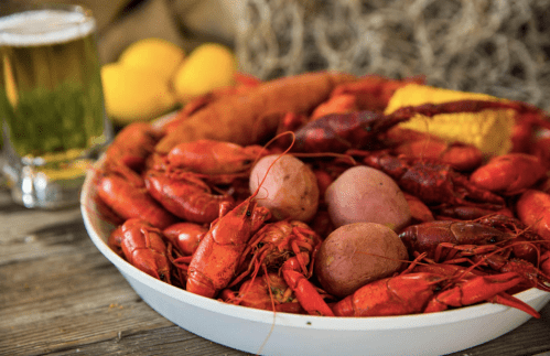A platter of boiled crawfish, potatoes, and corn, with a glass of beer and lemons in the background.