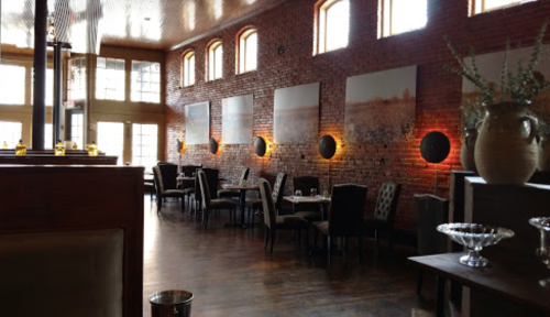 Cozy restaurant interior with brick walls, art on display, and warm lighting illuminating the dining area.