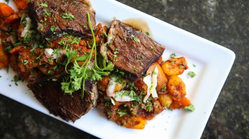 A plate of grilled meat topped with herbs, served with a colorful vegetable medley.