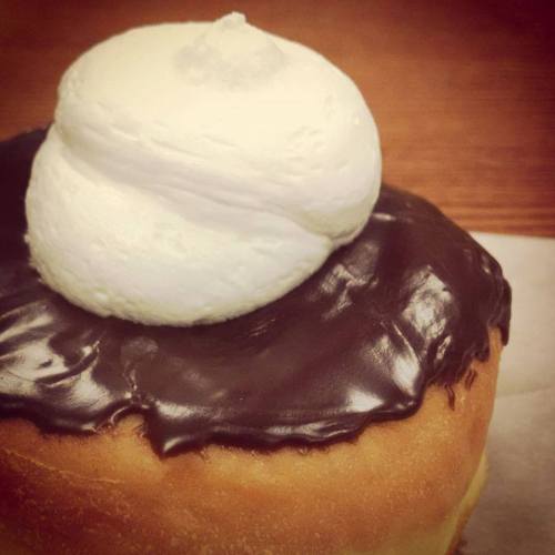 A close-up of a donut topped with chocolate icing and a swirl of whipped cream.