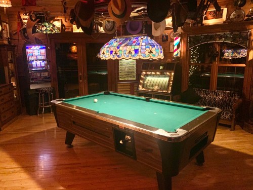 A cozy game room featuring a pool table, vintage jukebox, and colorful stained glass lamp, surrounded by wooden decor.