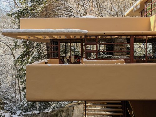 A modern architectural structure with a flat roof, covered in snow, surrounded by trees in a winter landscape.