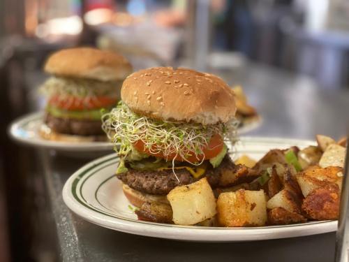 Two burgers with lettuce, tomato, and sprouts on sesame seed buns, served with crispy potato wedges on a plate.