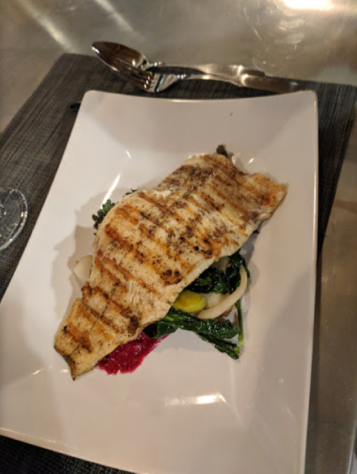 Grilled fish fillet served on a bed of sautéed greens and vegetables, garnished with a berry sauce.