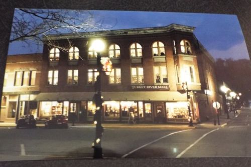 A historic brick building at dusk, featuring large windows and street lamps, with shops on the ground floor.