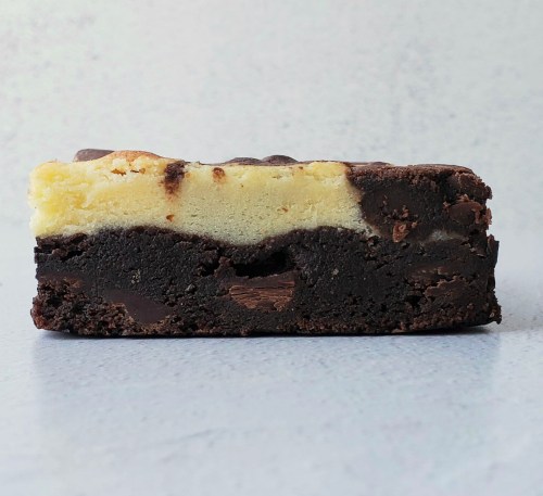 A close-up of a layered brownie with a dark chocolate base and a creamy cheesecake-like top.