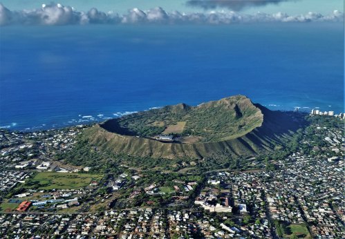 Aerial view of Diamond Head crater, surrounded by lush greenery and the ocean, with a coastal city in the background.