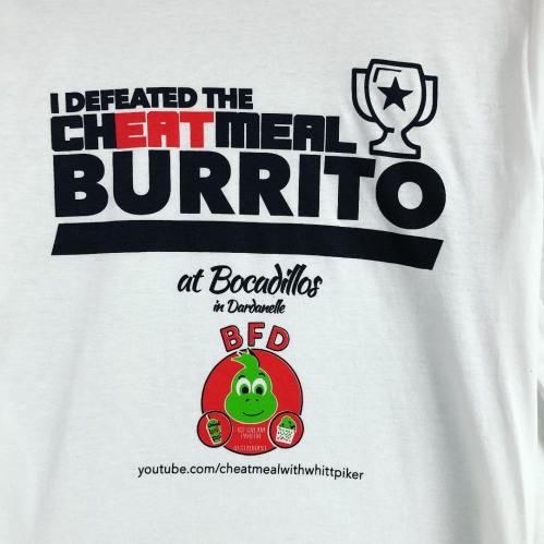 White t-shirt featuring text about defeating the "Cheat Meal Burrito" at Bocadillos, with a trophy graphic and logo.
