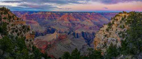 A panoramic view of the Grand Canyon at sunset, showcasing colorful rock formations and lush greenery.