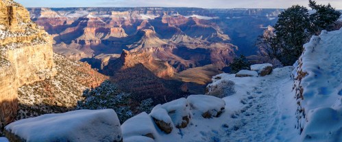 A snowy path winds through the Grand Canyon, showcasing layered rock formations and a vast, scenic landscape.