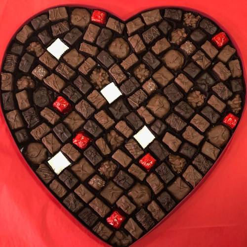 A heart-shaped box filled with assorted chocolates, featuring various shapes and colors, including red and white pieces.