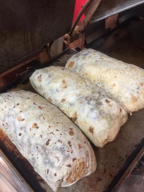 Three large, golden-brown burritos resting on a grill, with crispy, slightly charred tortillas.