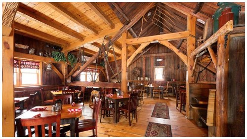 Cozy wooden restaurant interior with rustic decor, wooden beams, tables, and chairs, creating a warm atmosphere.