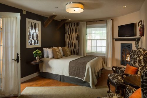 Cozy bedroom with a queen bed, decorative curtains, a fireplace, and stylish armchairs. Warm, inviting atmosphere.