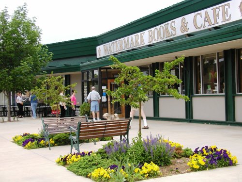 A bookstore and café with outdoor seating, surrounded by colorful flower beds and people enjoying the space.