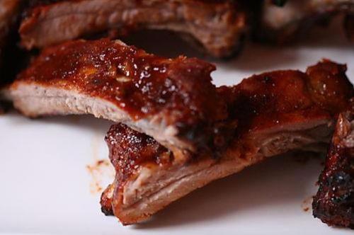 Close-up of succulent, glazed barbecue ribs on a white plate, showcasing a rich, caramelized sauce.