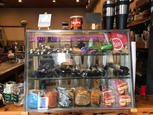 Display case filled with various snacks, bagels, and coffee supplies in a cozy café setting.