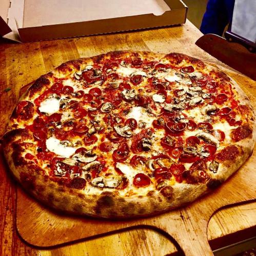 A freshly baked pizza topped with pepperoni, mushrooms, and melted cheese on a wooden cutting board.