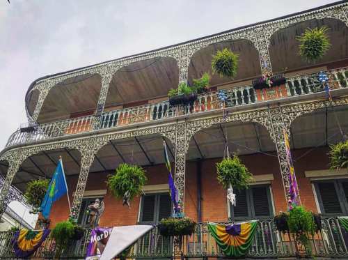 A historic building with ornate ironwork balconies adorned with plants and colorful decorations, typical of New Orleans.
