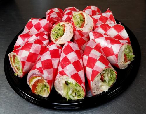 A platter of rolled sandwiches wrapped in red and white checkered paper, filled with lettuce, tomato, and turkey.