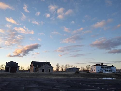 Abandoned buildings under a colorful sky with scattered clouds, set against a clear horizon.
