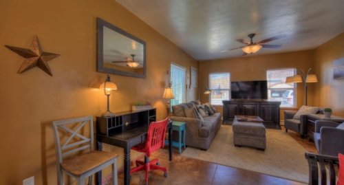 Cozy living room with a brown wall, comfortable seating, a TV, and a small desk with colorful chairs.