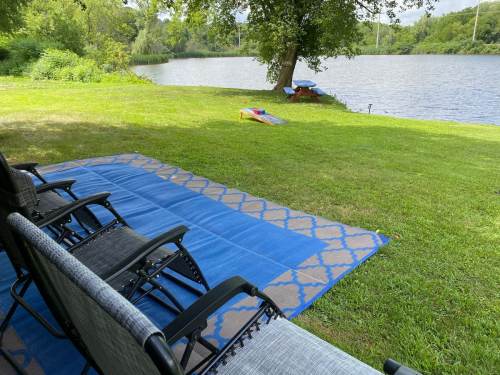 A peaceful lakeside scene with chairs on a blue mat, green grass, and a calm water view in the background.