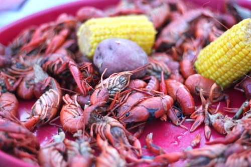 A vibrant platter of cooked crawfish, yellow corn, and a purple potato, showcasing a colorful seafood feast.