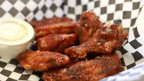 A basket of saucy chicken wings with a side of dipping sauce, lined with black and white checkered paper.
