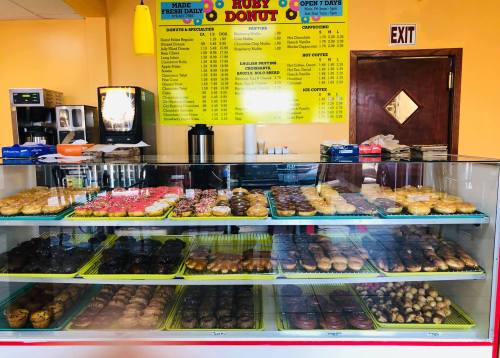 A display case filled with various donuts, including glazed, chocolate, and frosted options, in a bright donut shop.
