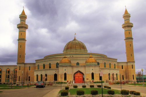 A large mosque with a golden dome and two tall minarets, set against a cloudy sky.