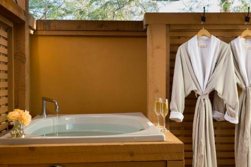 A serene spa setting featuring a hot tub, two bathrobes hanging, and two glasses of champagne on a wooden surface.