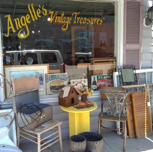 A storefront display featuring vintage items, including chairs, signs, and decorative pieces, outside Angelle's Vintage Treasures.