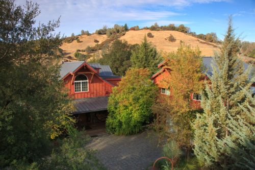 A scenic view of red wooden buildings surrounded by trees and hills under a clear blue sky.