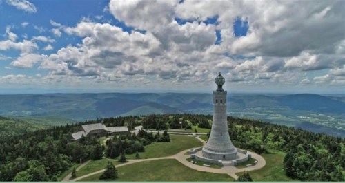 Aerial view of a tall tower surrounded by lush greenery and mountains under a cloudy sky.