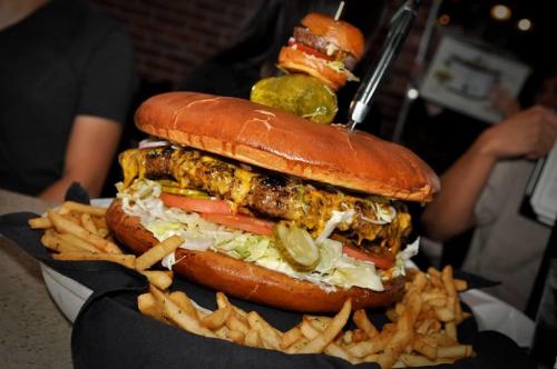 A giant burger with cheese, lettuce, tomatoes, and pickles, served with a side of fries.