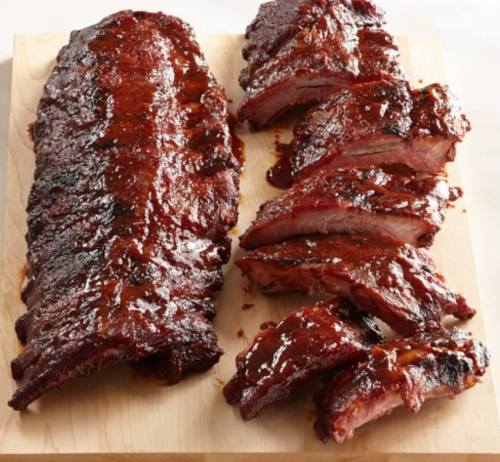 A wooden board with a whole rack of glazed ribs and several sliced pieces, showcasing a rich, shiny barbecue sauce.