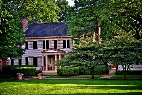 A charming two-story house surrounded by lush greenery and well-maintained landscaping on a sunny day.