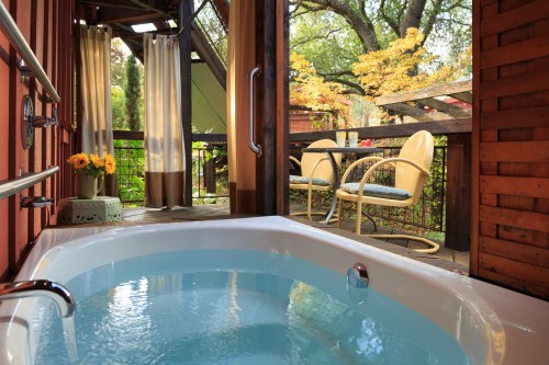A cozy outdoor space featuring a hot tub, wooden walls, and a view of lush greenery and autumn trees.