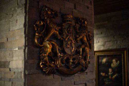 A golden coat of arms featuring two lions, mounted on a stone wall, with a framed painting nearby.
