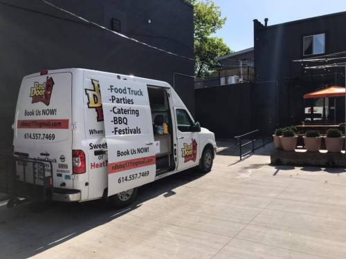 A food truck parked in an outdoor area, promoting BBQ catering and events with contact information displayed.