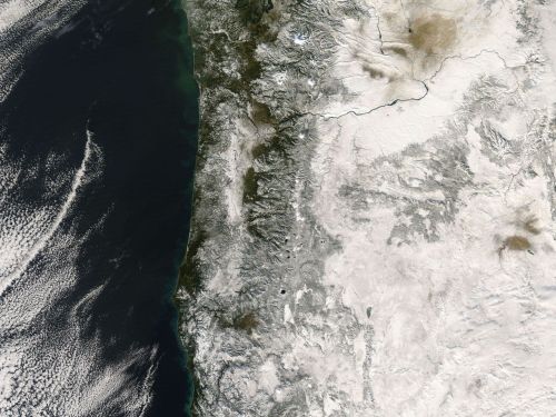 Satellite image showing a coastal region with mountains and varying terrain, featuring land and ocean contrasts.