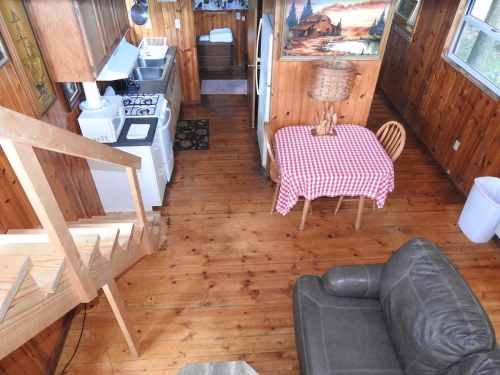 Cozy wooden cabin interior featuring a kitchen, dining table, and living area with a staircase.